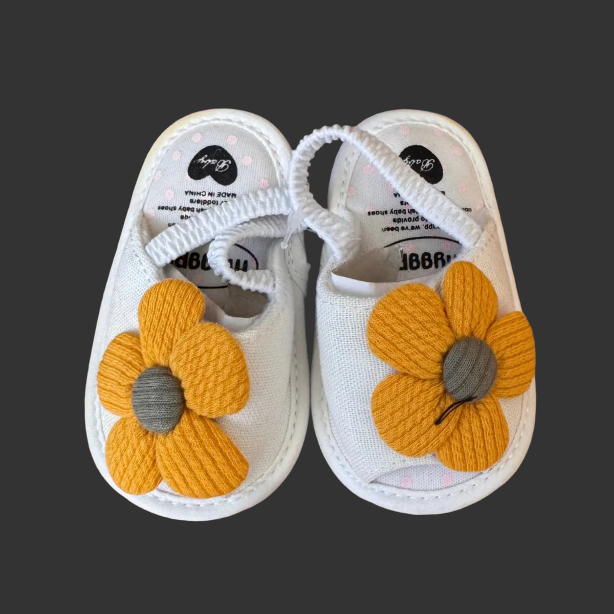 Pair of baby sandals with yellow flower designs on a wooden floor