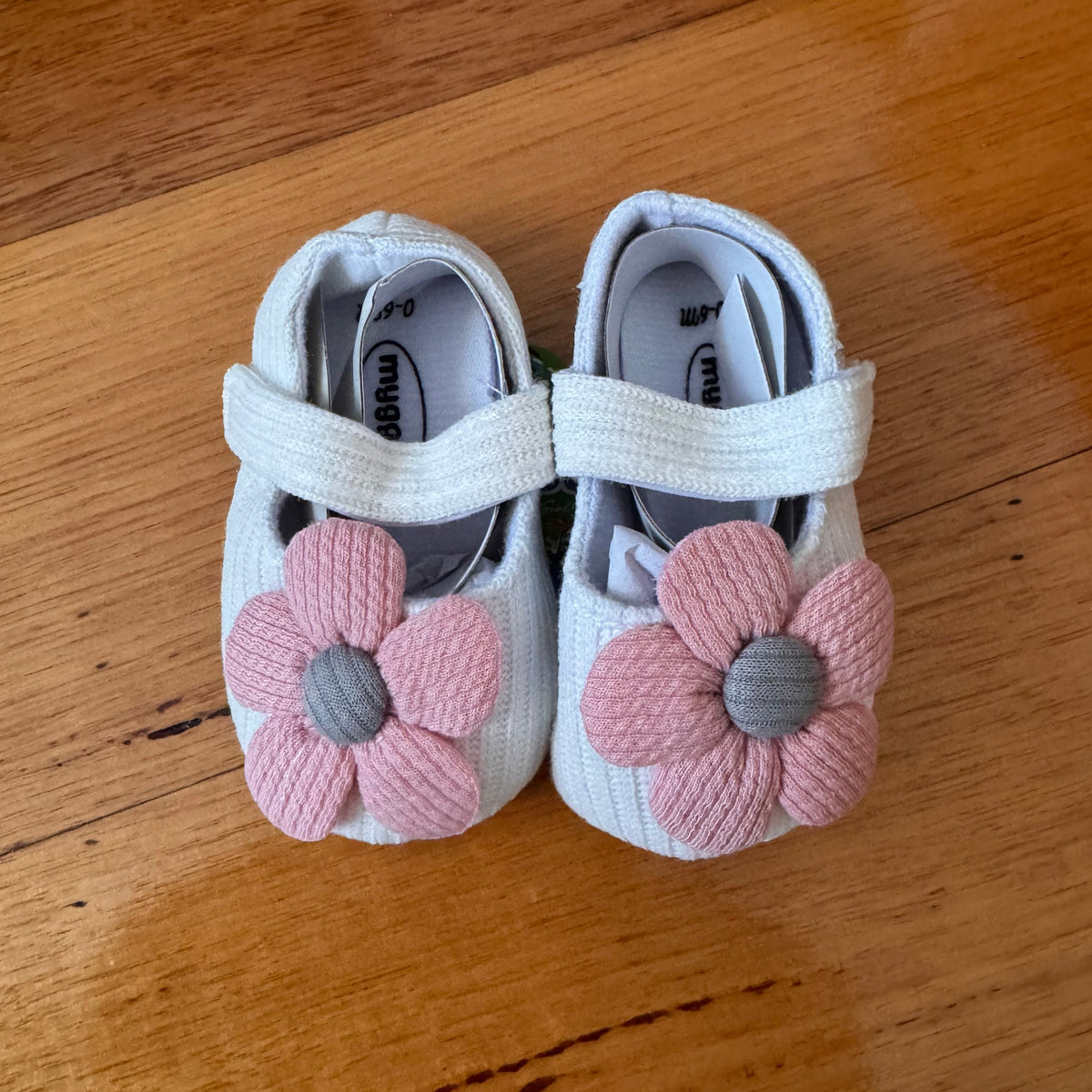 Pair of baby shoes with pink flower decorations on a wooden surface
