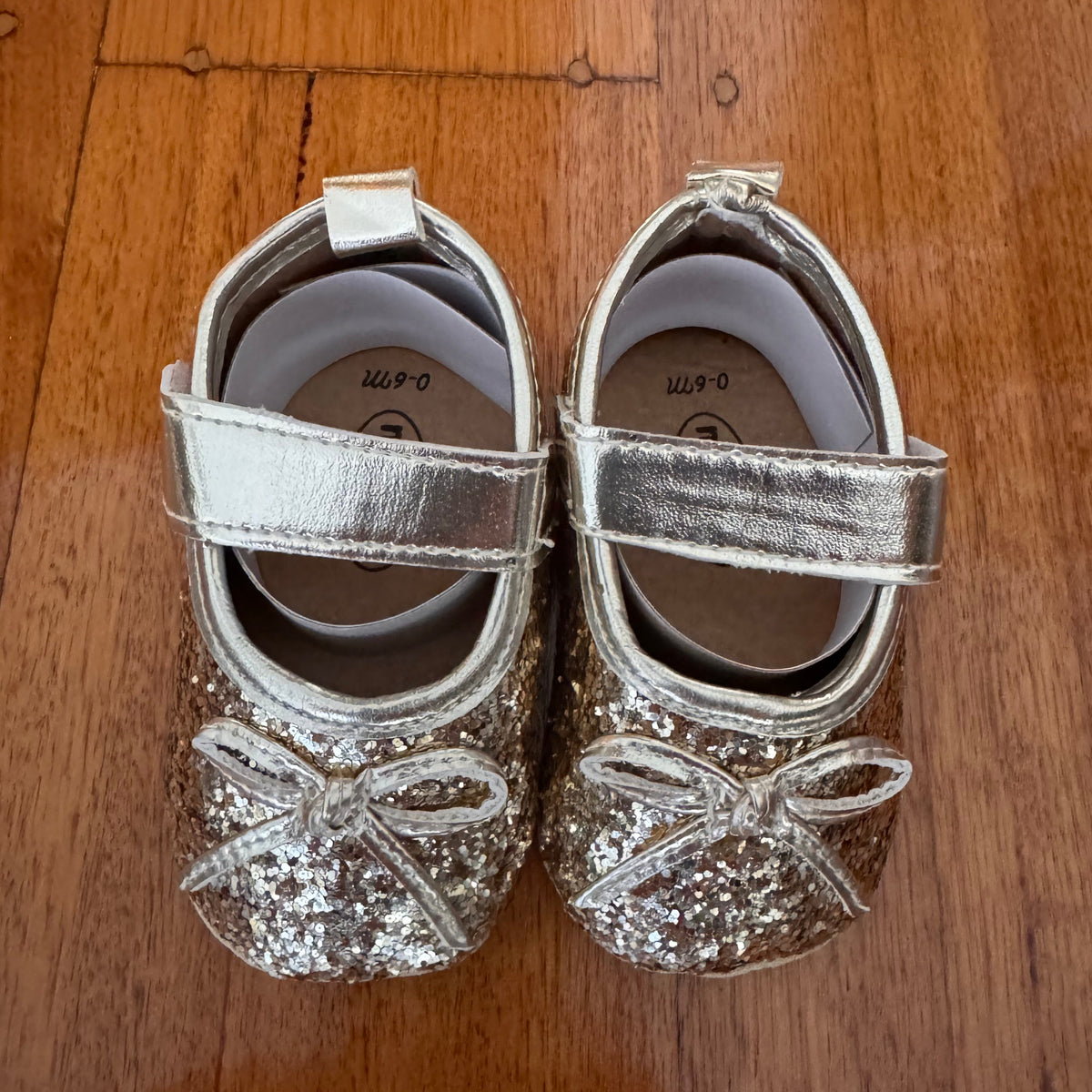 Pair of silver glittery baby shoes on a wooden surface