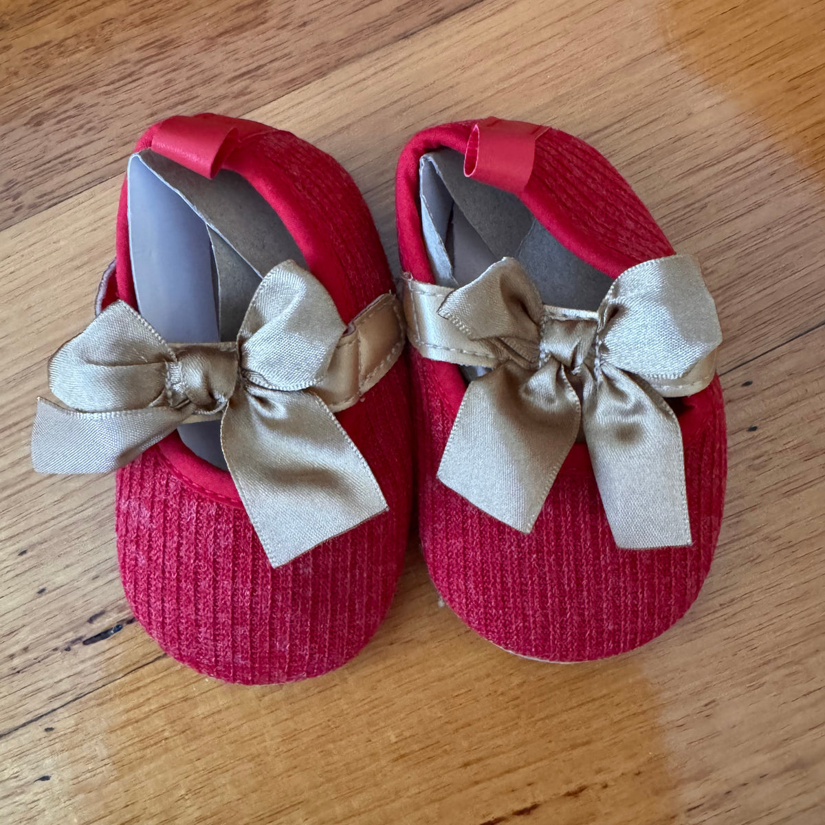 Red baby shoes with beige bows on a wooden floor